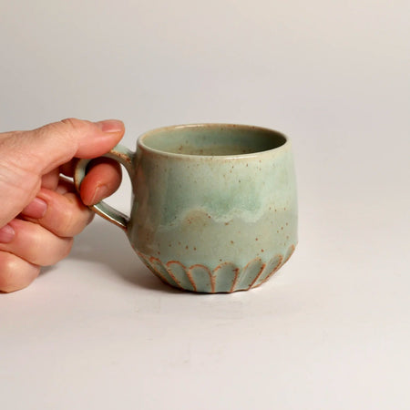 Hand holding a green ceramic mug against a plain white background