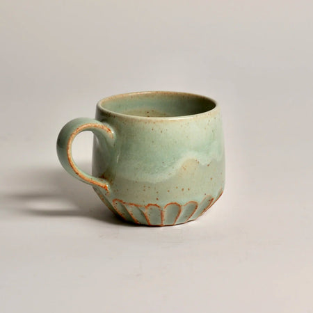 Green ceramic mug with decorative base on a light grey background