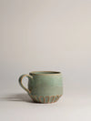Green ceramic mug with a carved bottom, on a white background