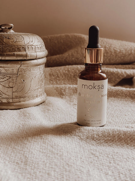 Bottle of moksa facial oil on a textured surface with an ornate container in the background