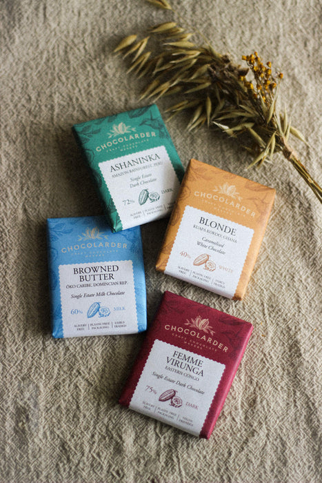 Four mini chocolate bars in various colours and flavours on a beige linen surface with dried flowers 