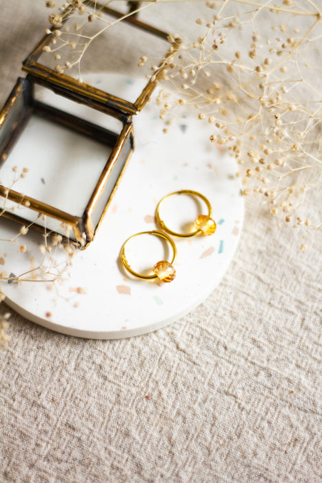 Gold hoop earrings with citrine beads on a terazzo surface with a textured beige linen  background