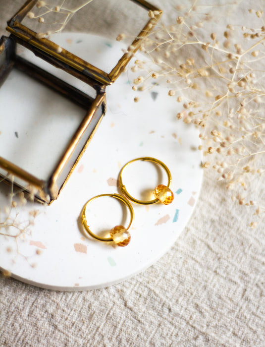 Gold hoop earrings with citrine beads on a white plate with a linen background