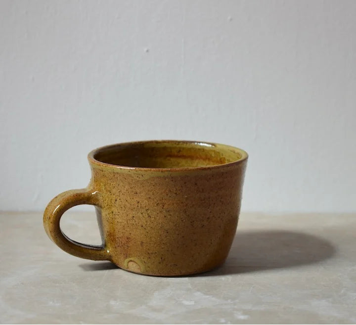 Brown ceramic mug on a light grey surface with a plain background