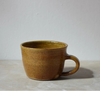 Brown ceramic mug on a light grey surface with a white background