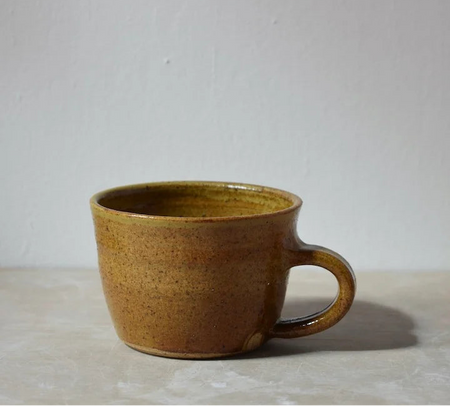 Brown ceramic mug on a light grey surface with a white background