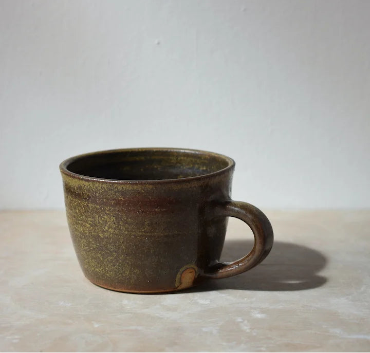 dark green ceramic mug on a light surface with a grey background