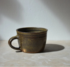 dark green ceramic mug on a light surface with a grey background