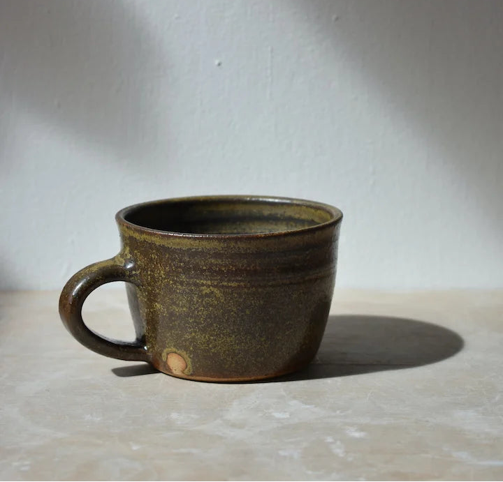dark green ceramic mug on a light surface with a grey background