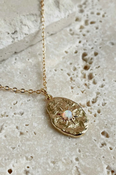 A gold necklace with an oval pendant featuring an oplalite stone, on a stone surface