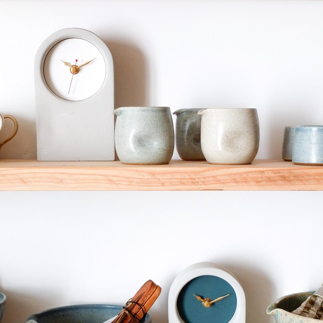 Shelf with ceramic mugs, clocks, and decorative items against a white wall.