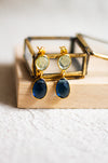 Pair of gold earrings with blue stones on a wooden surface and a neutral linen background
