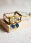 Gold earrings with blue and green gemstones on a wooden stand