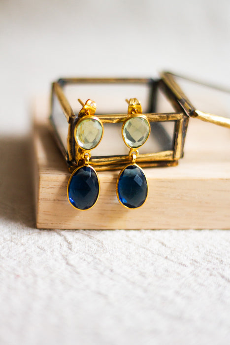 Pair of gold earrings with blue stones on a wooden surface and a neutral linen background