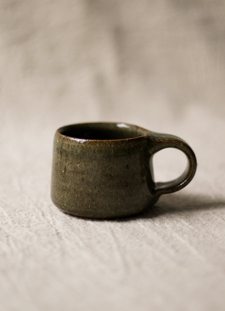 Dark green ceramic espresso cup on a beige linen surface