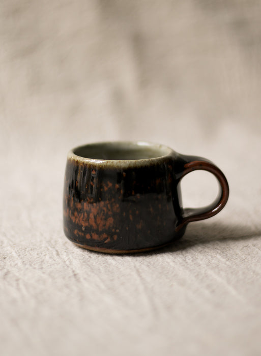 Brown ceramic espresso cup on a beige linen background