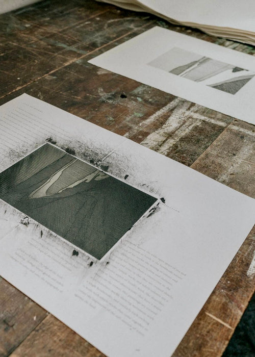 Etching prints on paper with printing plate next to them on a wooden table 