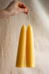 Two beesawx candles held by a hand against a beige background