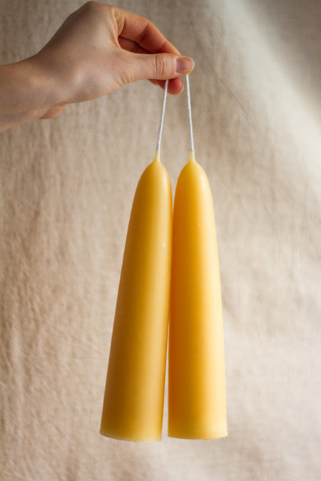Two beesawx candles held by a hand against a beige background