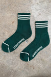 Green socks with white stripes and 'LEBON SHOPPE' branding on a concrete surface