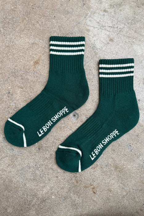Green socks with white stripes and 'LEBON SHOPPE' branding on a concrete surface