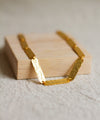 Gold textured necklace on a wooden block with a neutral background