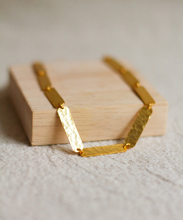 Gold textured necklace on a wooden block with a neutral background
