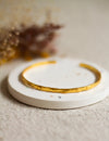 Gold bangle on a white coaster with blurred dried flowers in the background