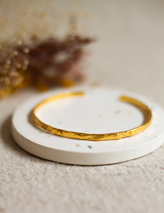 Gold bangle on a white coaster with blurred dried flowers in the background