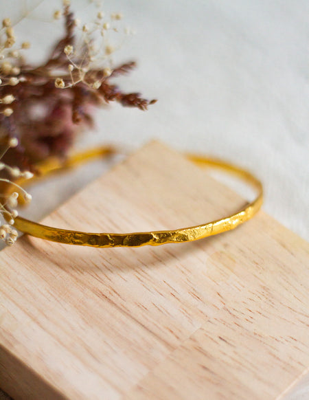 Gold bangle on a wooden surface with blurred dried flowers in the background