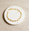 Gold hammered link bracelet on a round, terrazzo coaster with a beige linen background