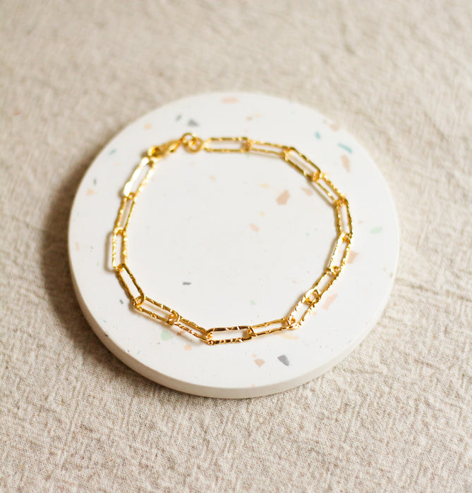 Gold hammered link bracelet on a round, terrazzo coaster with a beige linen background