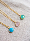 Three gold necklaces with muted teardrop shaped pendants on a neutral linen surface