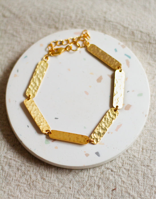 Gold textured bracelet on a round, speckled white coaster with a beige linen background