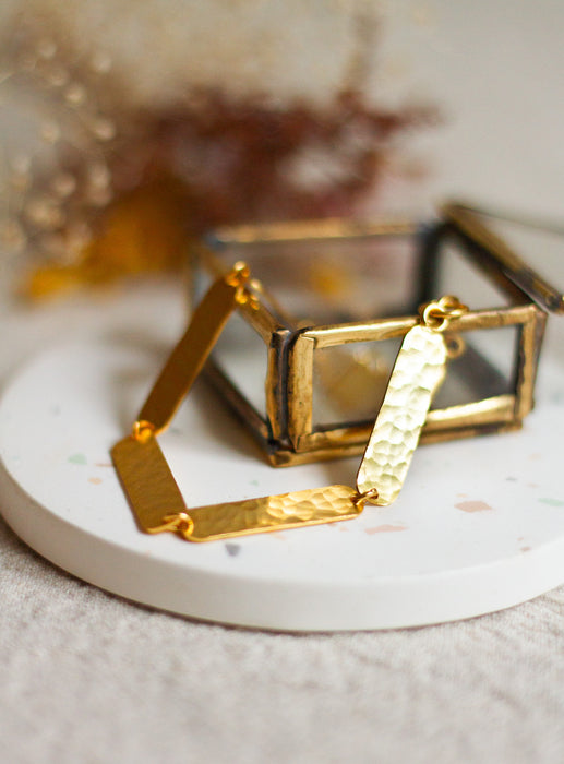 Gold textured bracelet on a white coaster with a blurred background