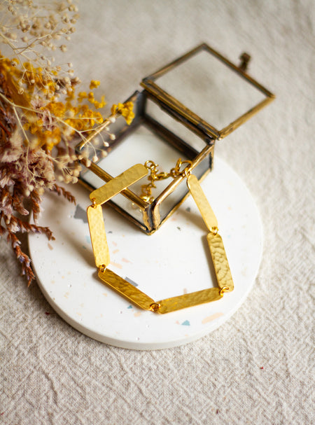 Gold textured bracelet on a white coaster with dried flowers on a beige linen surface