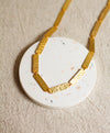 Gold textured necklace on a round, speckled coaster with a neutral background