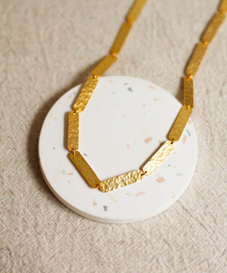 Gold textured necklace on a round, speckled coaster with a neutral background