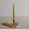 Two beeswax candles and a small brass candlestick holder on a neutral background