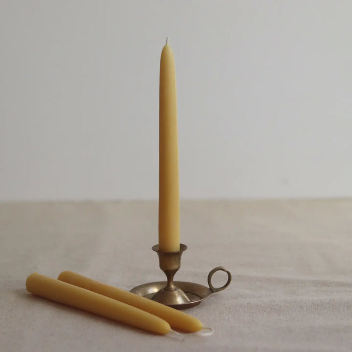 Two beeswax candles and a small brass candlestick holder on a neutral background