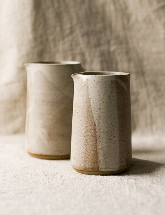 2 beige speckled ceramic pitchers with a textured surface on a neutral background