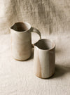 Two beige ceramic pitchers on a textured beige linen background 