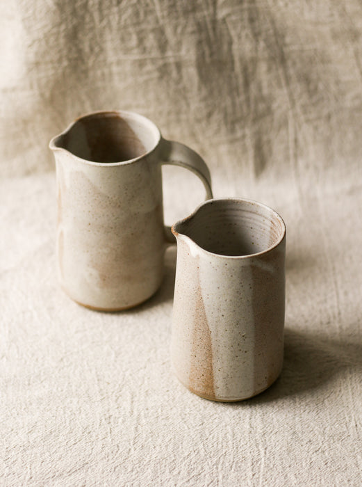 Two beige ceramic pitchers on a textured beige linen background 