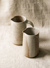 2 beige speckled ceramic pitchers with a textured surface on a neutral background