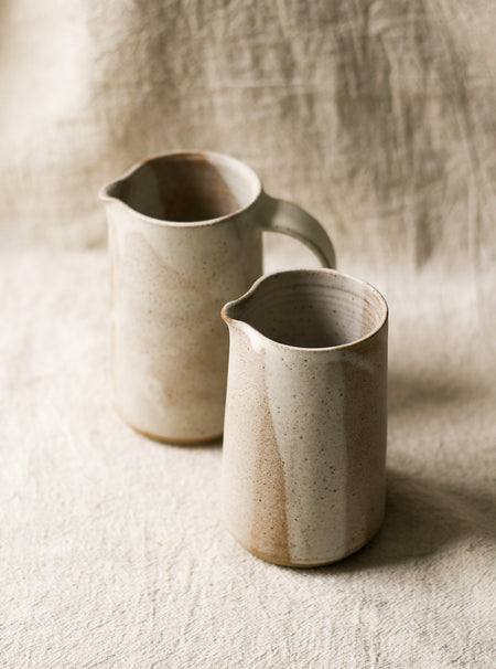 2 beige speckled ceramic pitchers with a textured surface on a neutral background