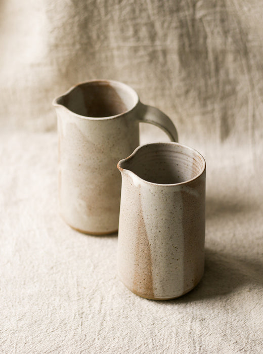 2 beige speckled ceramic pitchers with a textured surface on a neutral background