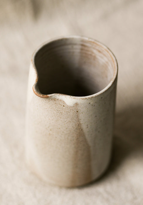 Beige speckled ceramic pitcher with a textured surface on a neutral background