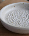 White ceramic garlic grater with textured surface on a wooden surface