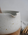 White speckled ceramic matcha bowl with a wooden spoon on a wooden cutting board.