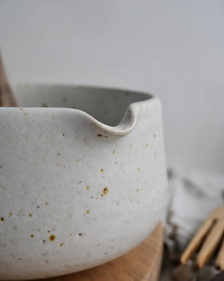 White speckled ceramic matcha bowl with a wooden spoon on a wooden cutting board.